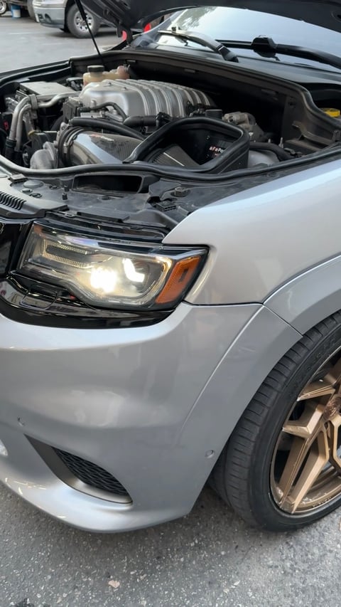 Silver car with open hood displaying a large supercharged V8 engine with intake manifold visible