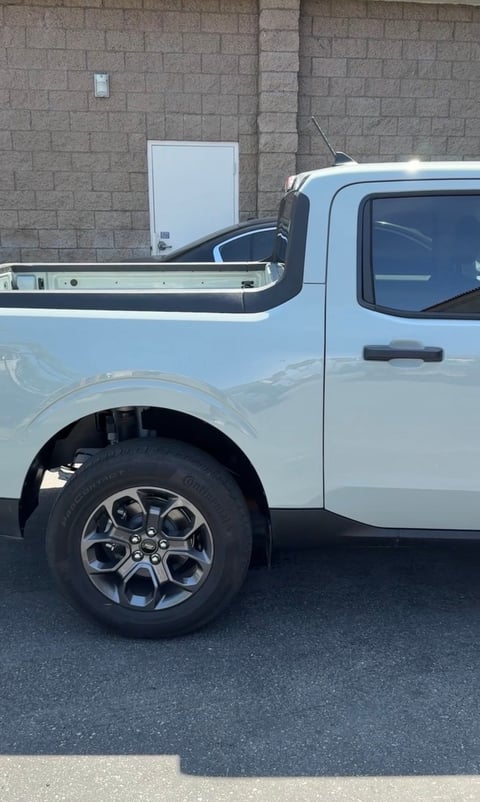 White pickup truck parked against brick building, side view showing bed, wheel, and window