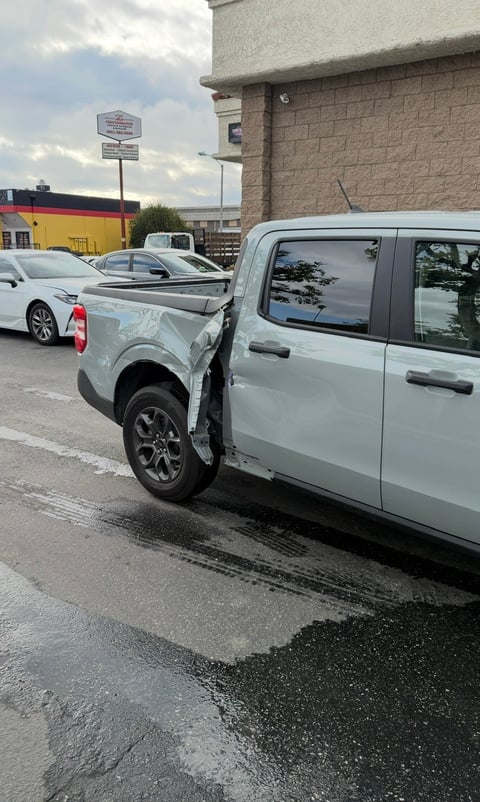 Two white vehicles damaged in a parking lot collision, with a brick building and commercial storefront visible in the background