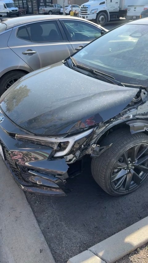 Damaged black sedan with crumpled front end in parking lot collision scene