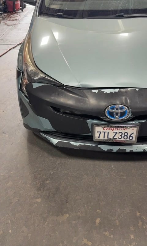 Front view of a damaged white Toyota vehicle with crumpled bumper and broken headlight on a driveway