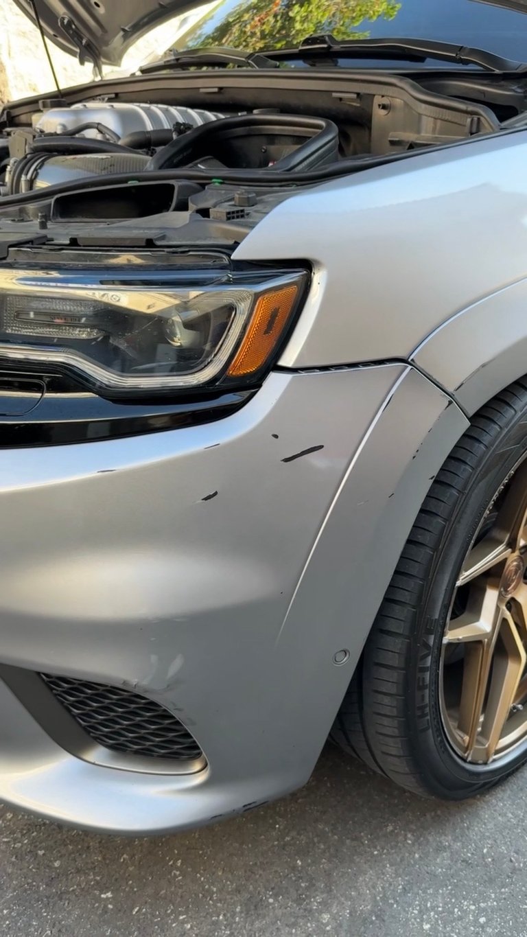 Silver SUV with open hood showing engine, parked with headlight and tire visible in daylight