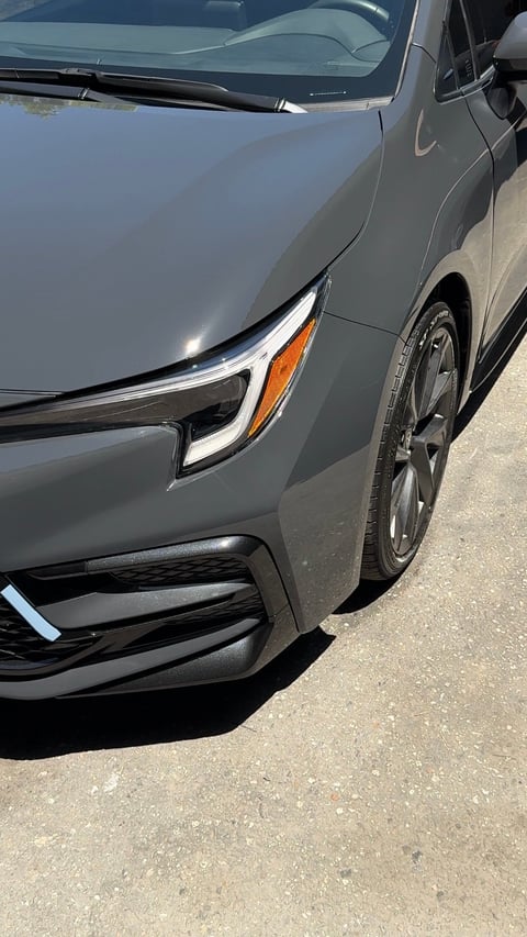 Silver sedan parked on pavement showing front quarter view with LED headlight, orange turn signal, and wheel detail