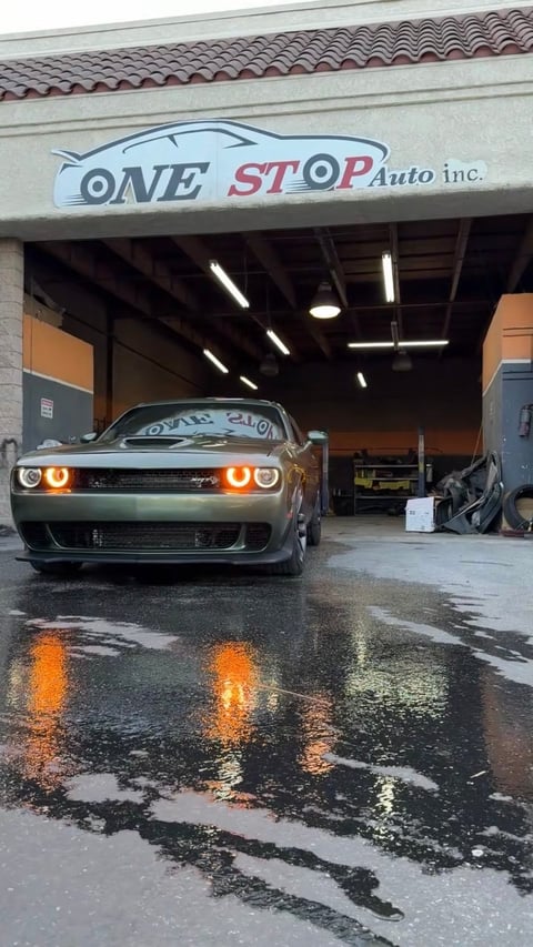 Silver Dodge Challenger with illuminated orange headlights parked in One Stop Auto garage with wet floor