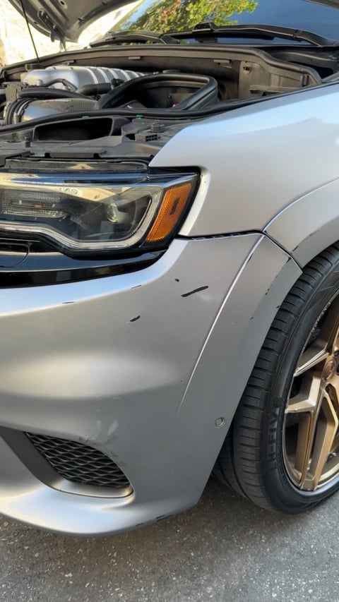 Silver SUV with open hood showing engine compartment, headlight and tire visible from front angle view